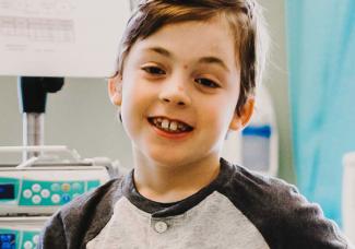 A young boy in a hospital bed smiling at the camera.
