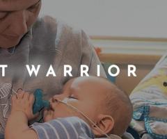 A mother holding a baby boy with a soother in his mouth. The words Heart Warrior overlay the image.