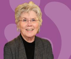 Photo of Carol Young on a purple background with light purple outlines of the W and K symbols from the IWK logo